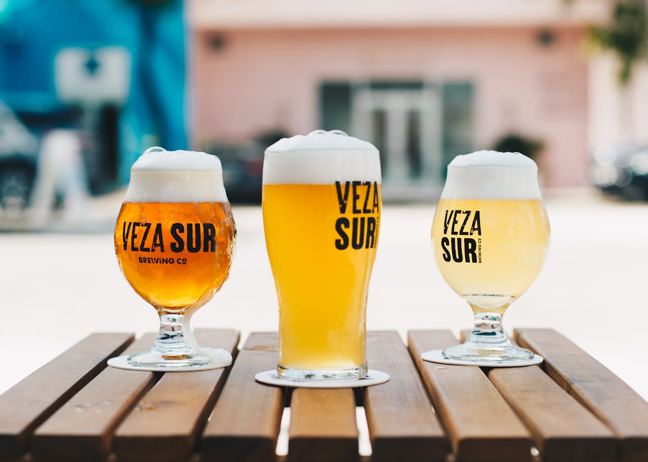 Close-up of three craft beers with frothy tops on a wooden table outdoors.